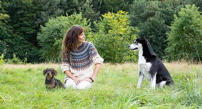 Tina Tschürtz sitzt im hohen Gras zwischen einem Dackel und einem schwarz-weißen Hund