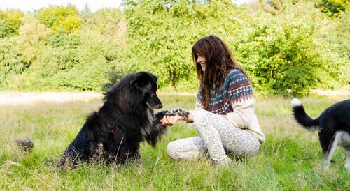Tina Tschürtz kniet im Gras vor einem großen schwarzen Hund